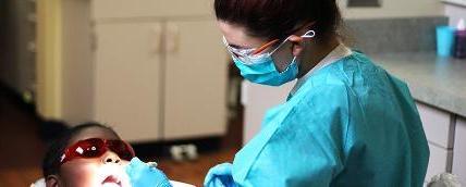 A dental student examining a child patient's mouth with a small flashlight